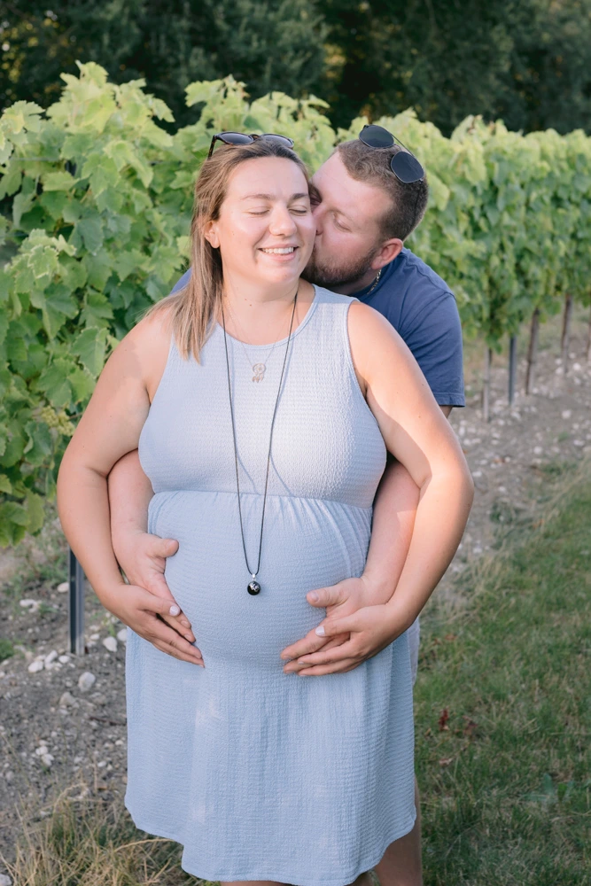 Séance photo de grossesse dans les vignes, futur papa embrassant sa compagne enceinte à Barbezieux-Saint-Hilaire par Alexandre Topolewski