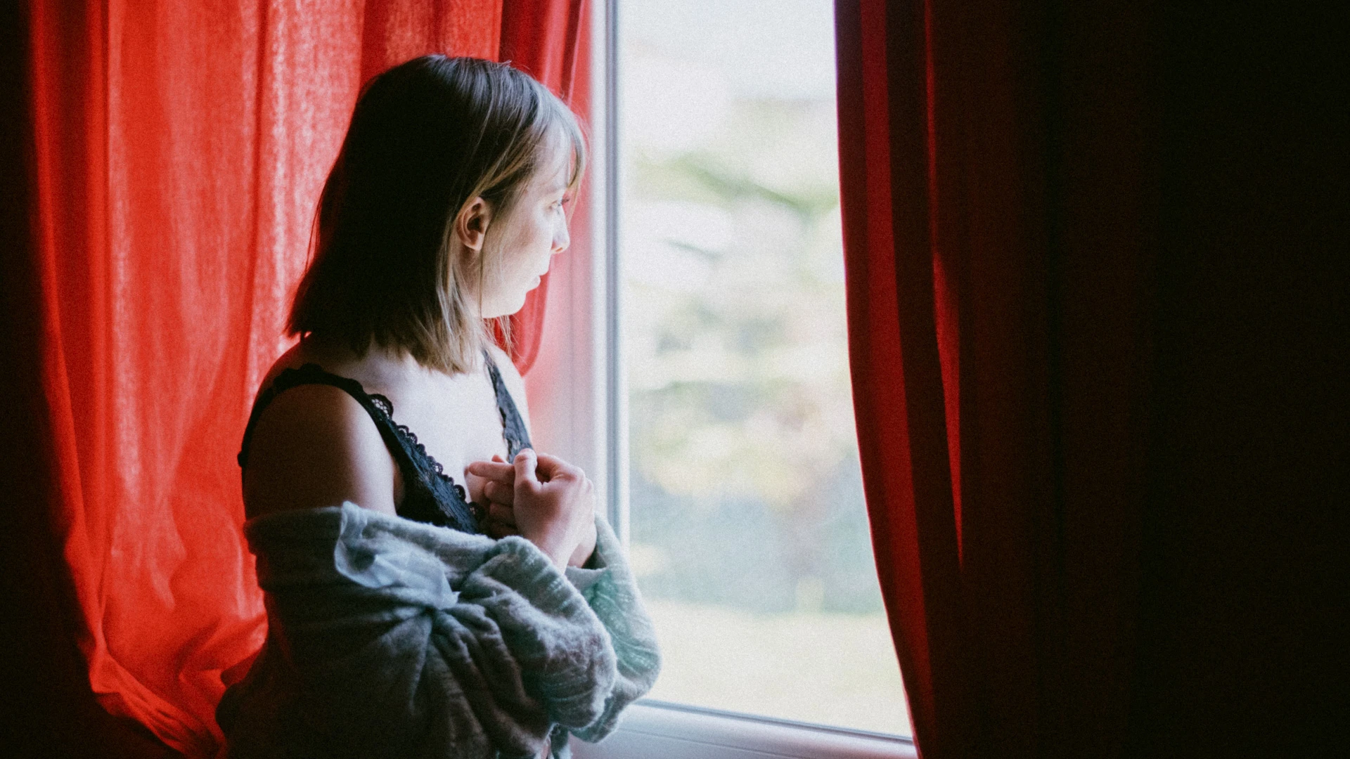 Portrait de femme à la fenêtre, entre des rideaux rouges, séance boudoir en Charente