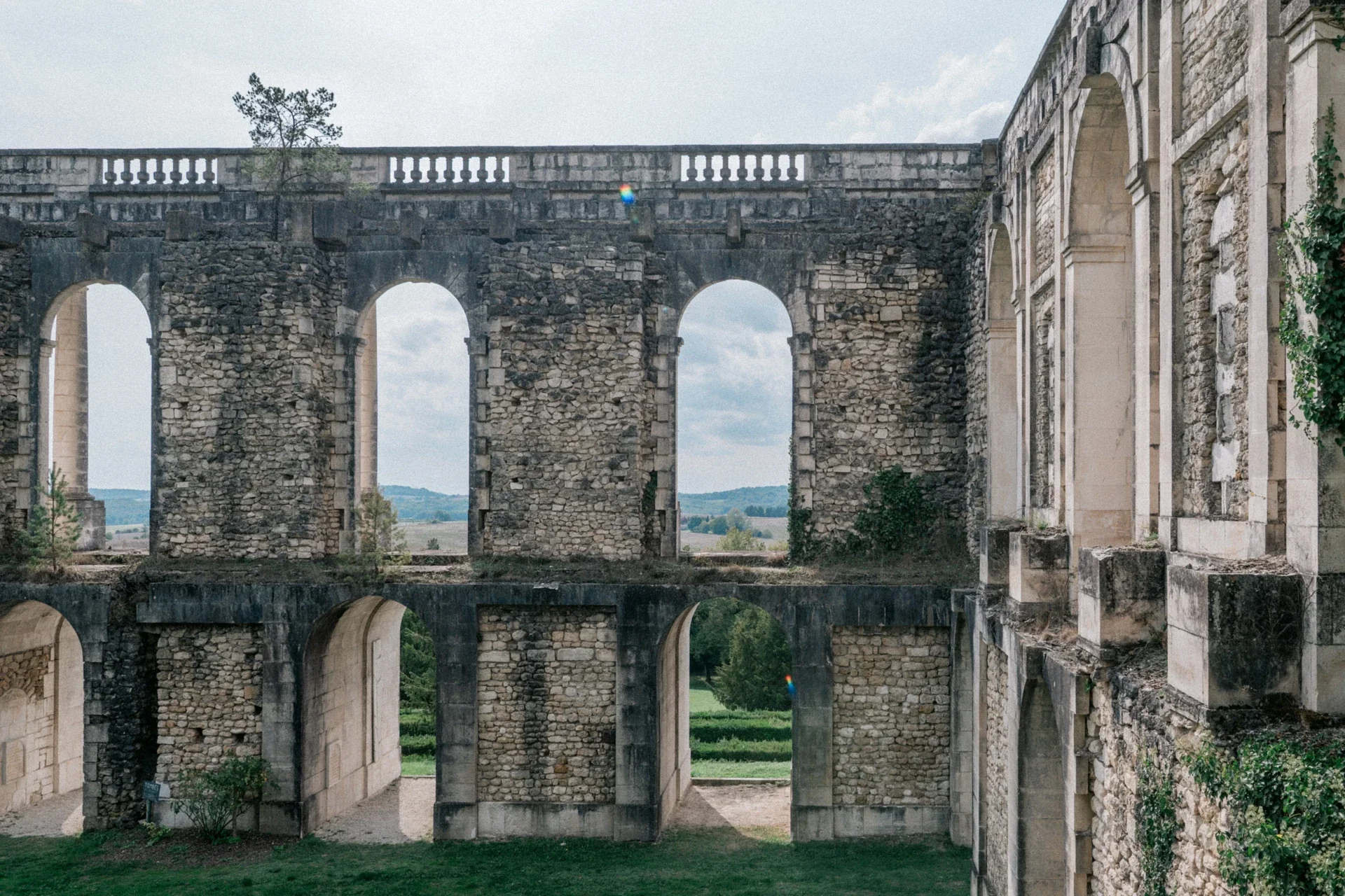 Arcades de pierre superposées ouvertes sur le ciel et la campagne, avec un balustre au sommet