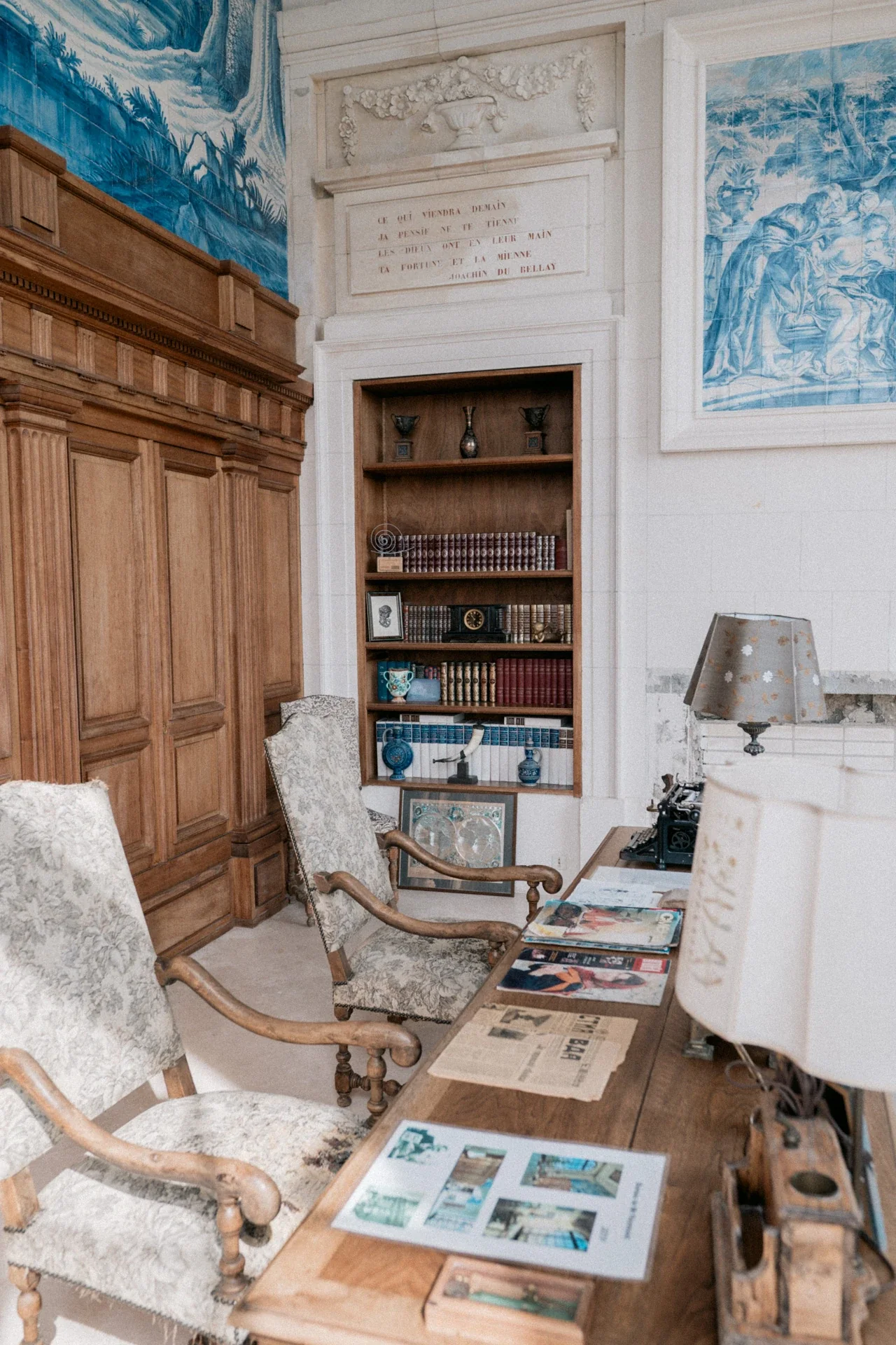 Alcôve de bibliothèque aux livres reliés, fauteuils anciens et bureau couvert de journaux, de revues et d'une machine à écrire