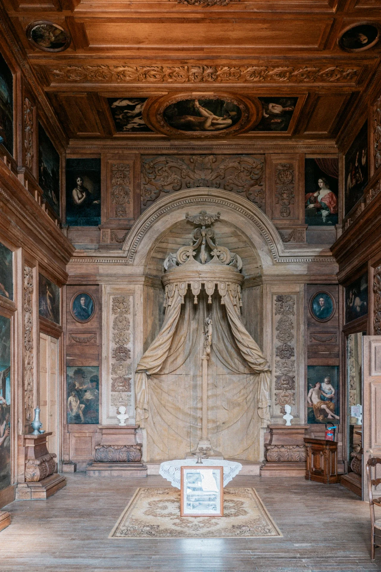 Chambre en bois sculpté avec alcôve à baldaquin, portraits peints, plafond à caissons et tapis au centre