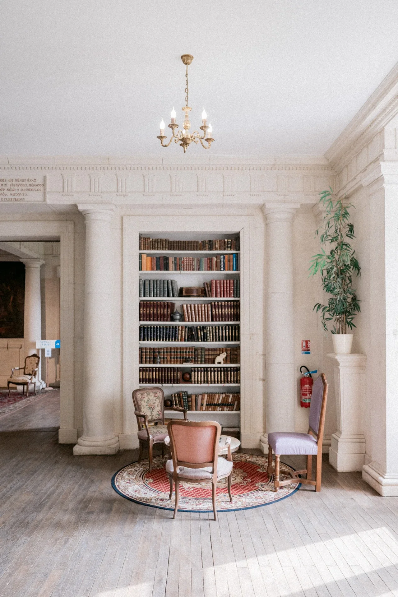 Coin de lecture entre deux colonnes de pierre, avec une bibliothèque encastrée, des chaises anciennes et un petit tapis rond