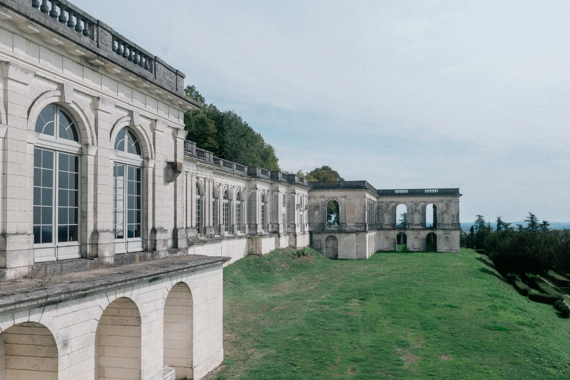 Galerie à arcades et façade en pierre claire du château de la Mercerie, dominant une pelouse et la campagne charentaise