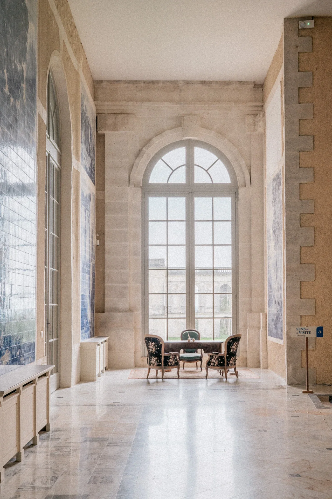 Galerie aux panneaux d'azulejos bleus et grande fenêtre cintrée, avec un petit salon de fauteuils en contrejour