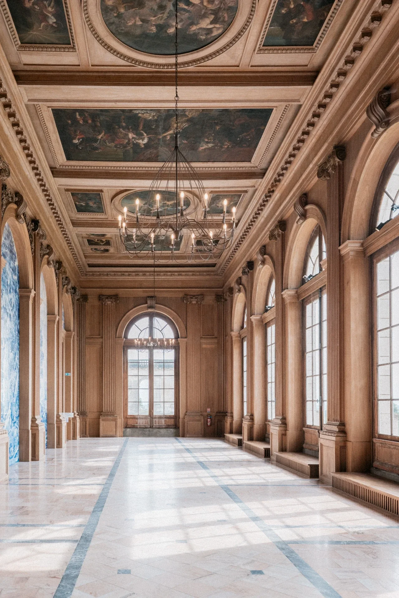 Galerie en bois clair, plafond à caissons peints, lustre à bougies et hautes fenêtres cintrées