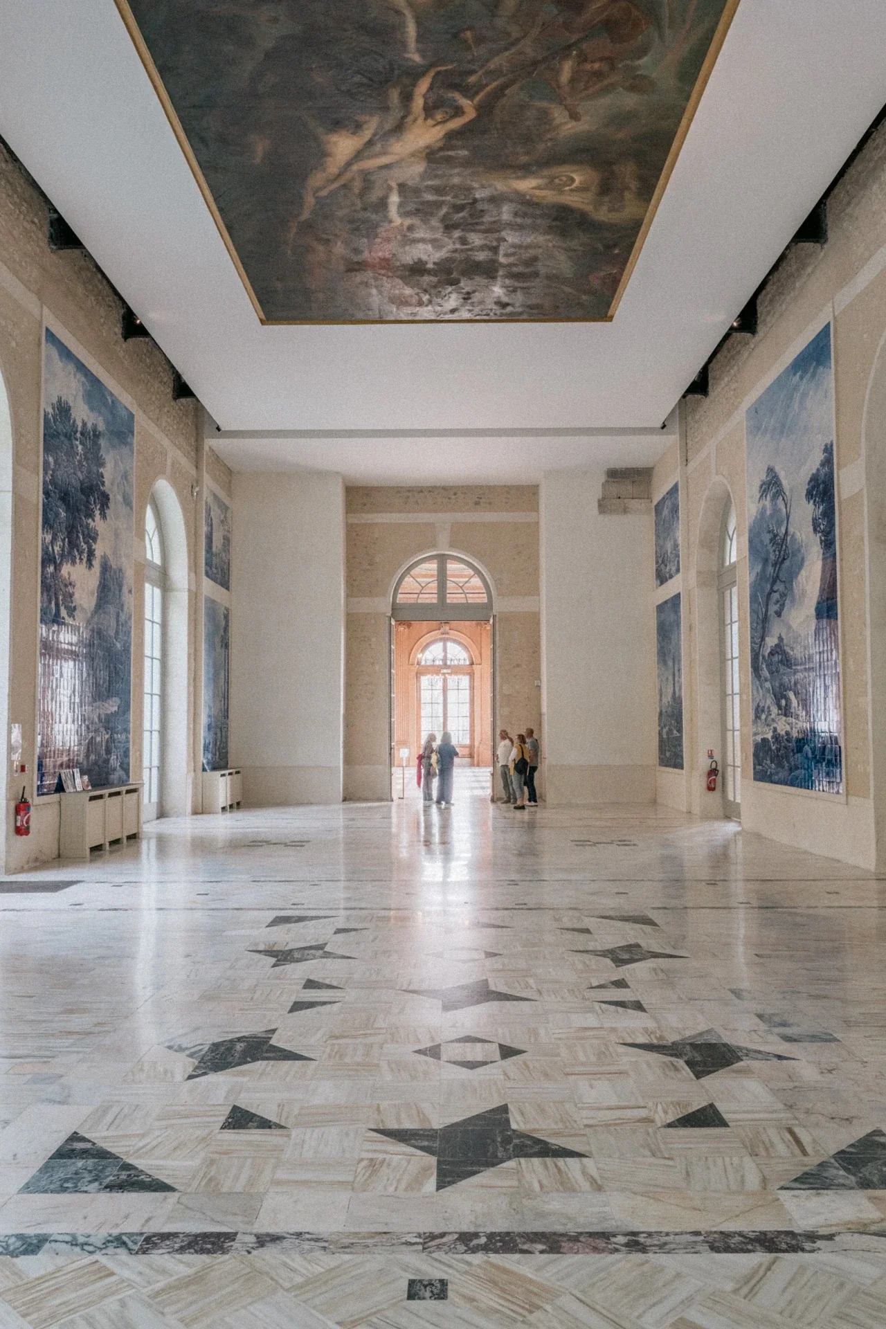 Grand hall au sol de marbre, plafond peint dans un cadre doré et panneaux d'azulejos bleus, avec des visiteurs au fond