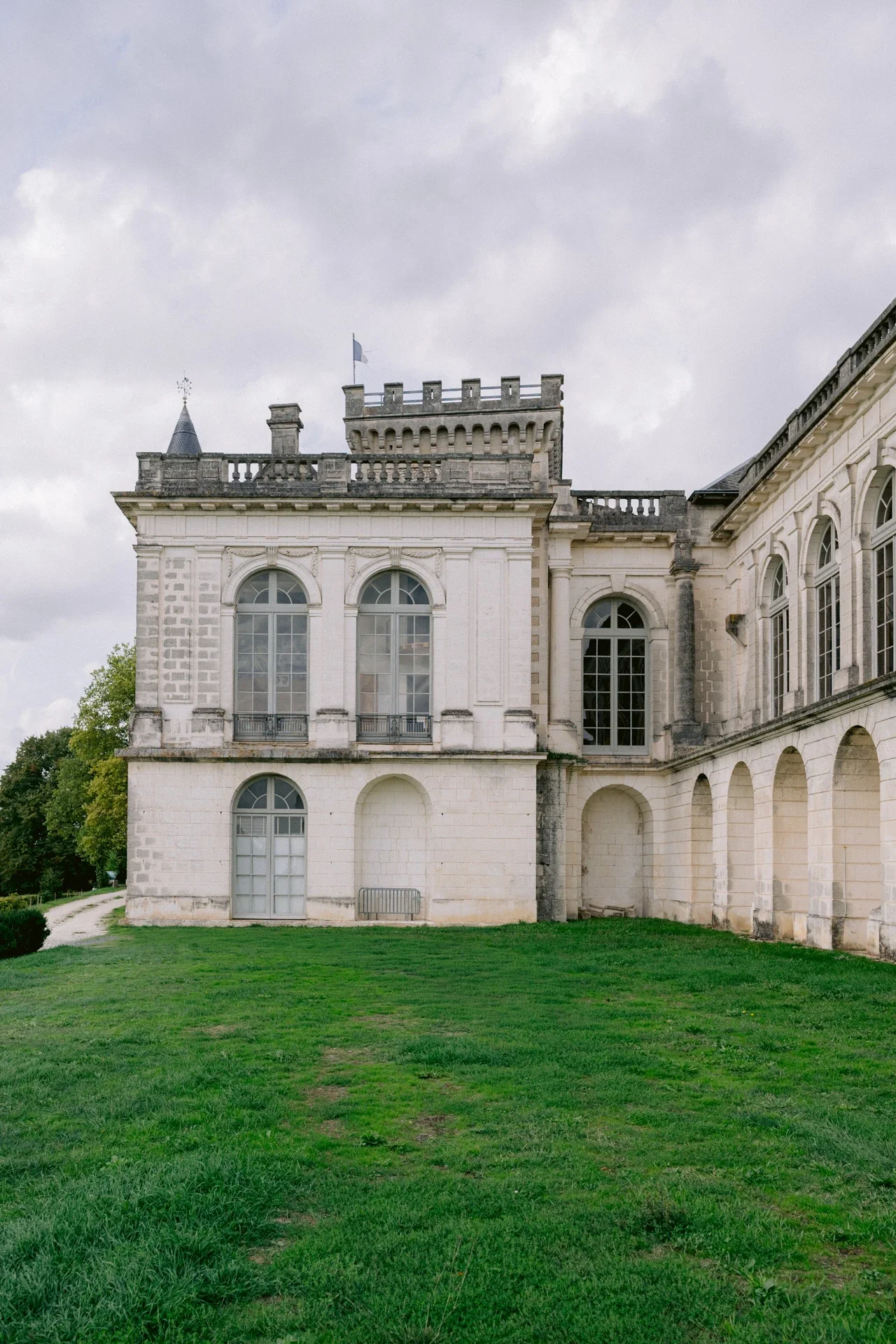 Pavillon d'angle aux grandes fenêtres cintrées, tour crénelée et drapeau, au-dessus d'une pelouse