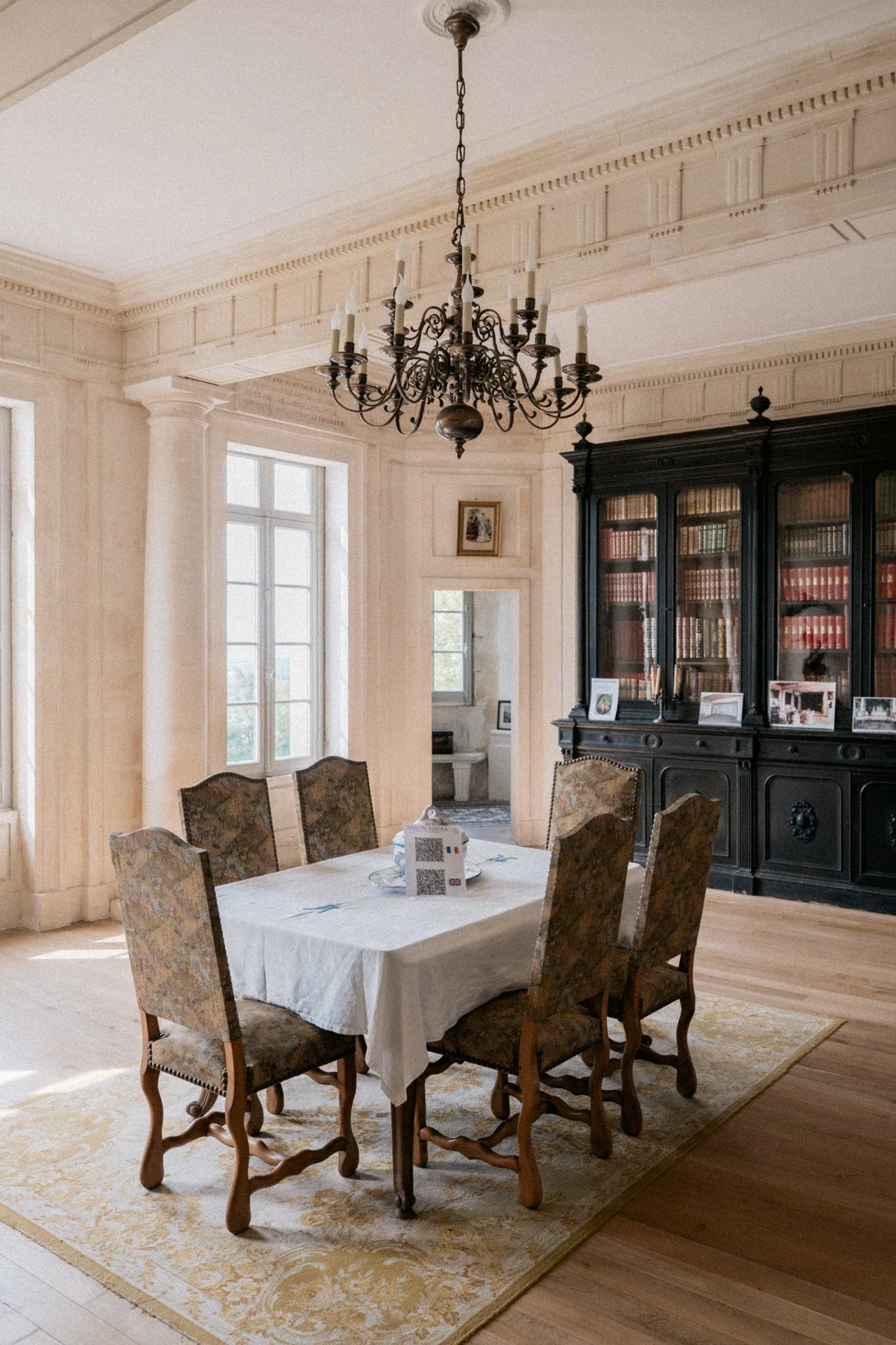 Table recouverte d'une nappe blanche sous un lustre en bronze, devant une bibliothèque vitrée noire