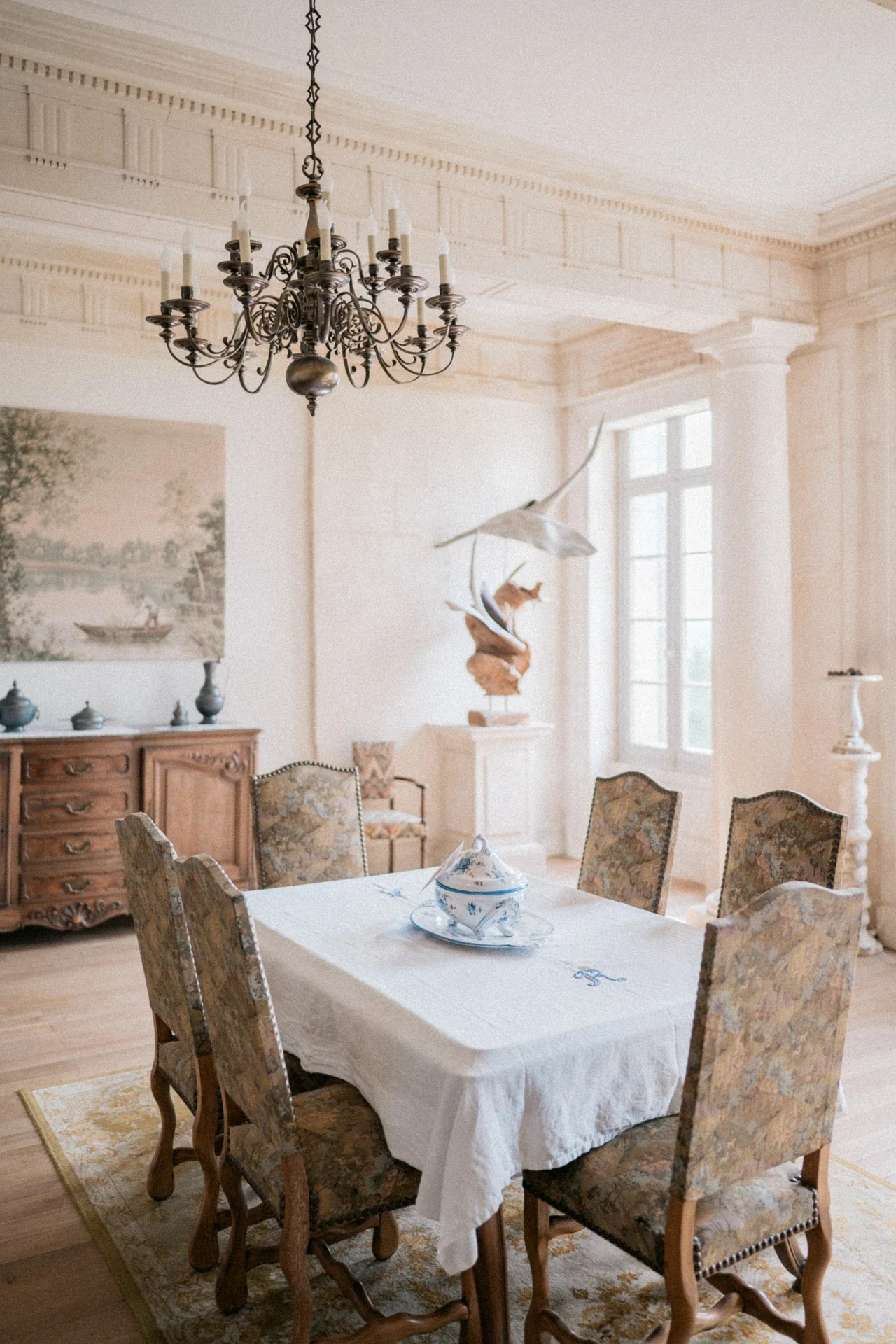 Soupière en faïence bleue sur une nappe brodée, entourée de chaises tapissées, dans un salon clair