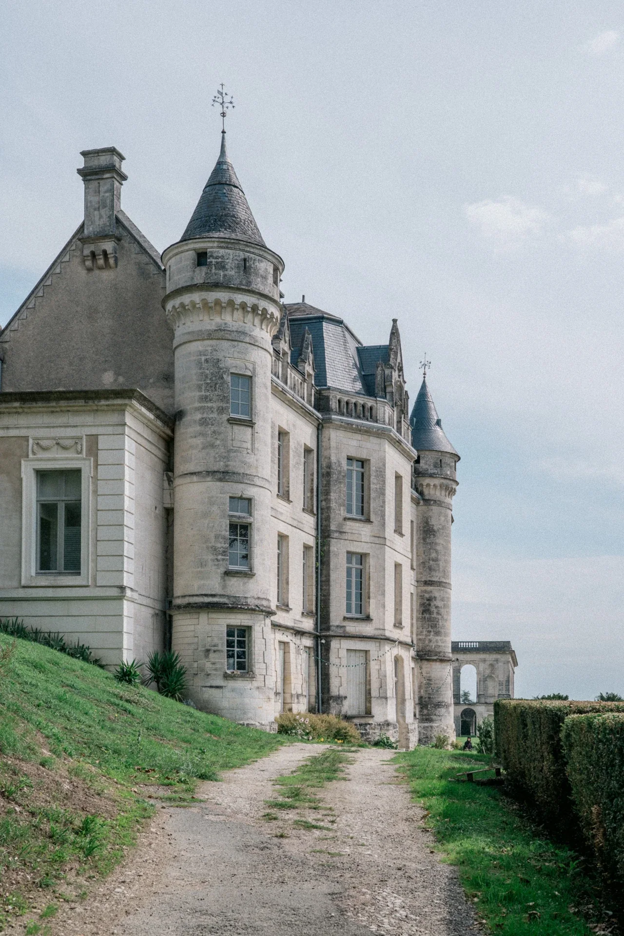 Tourelles à toit d'ardoise et façade en pierre patinée du château de la Mercerie, avec un chemin de gravier au premier plan