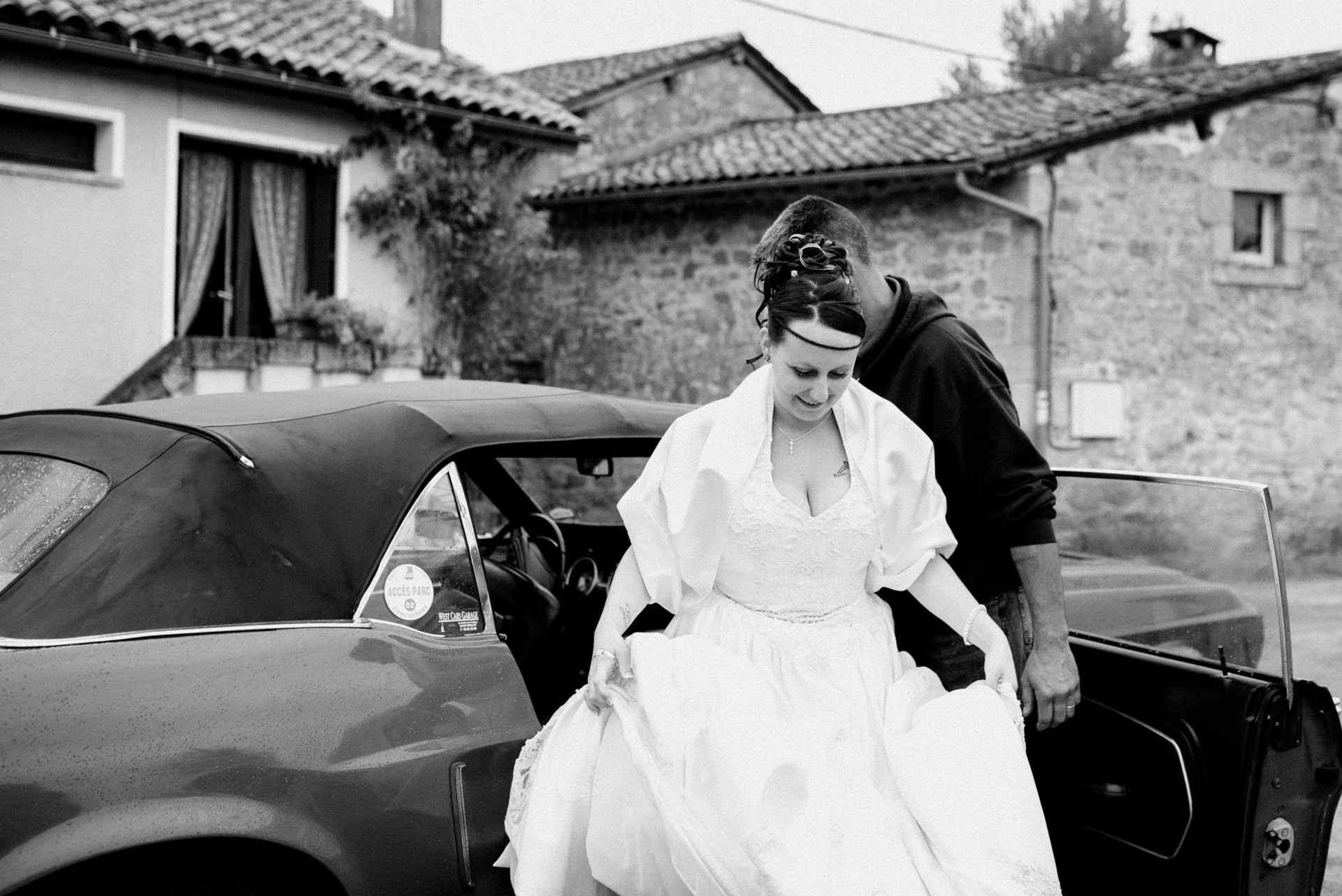 Mariée descendant de la Mustang en retenant sa robe, photographie en noir et blanc