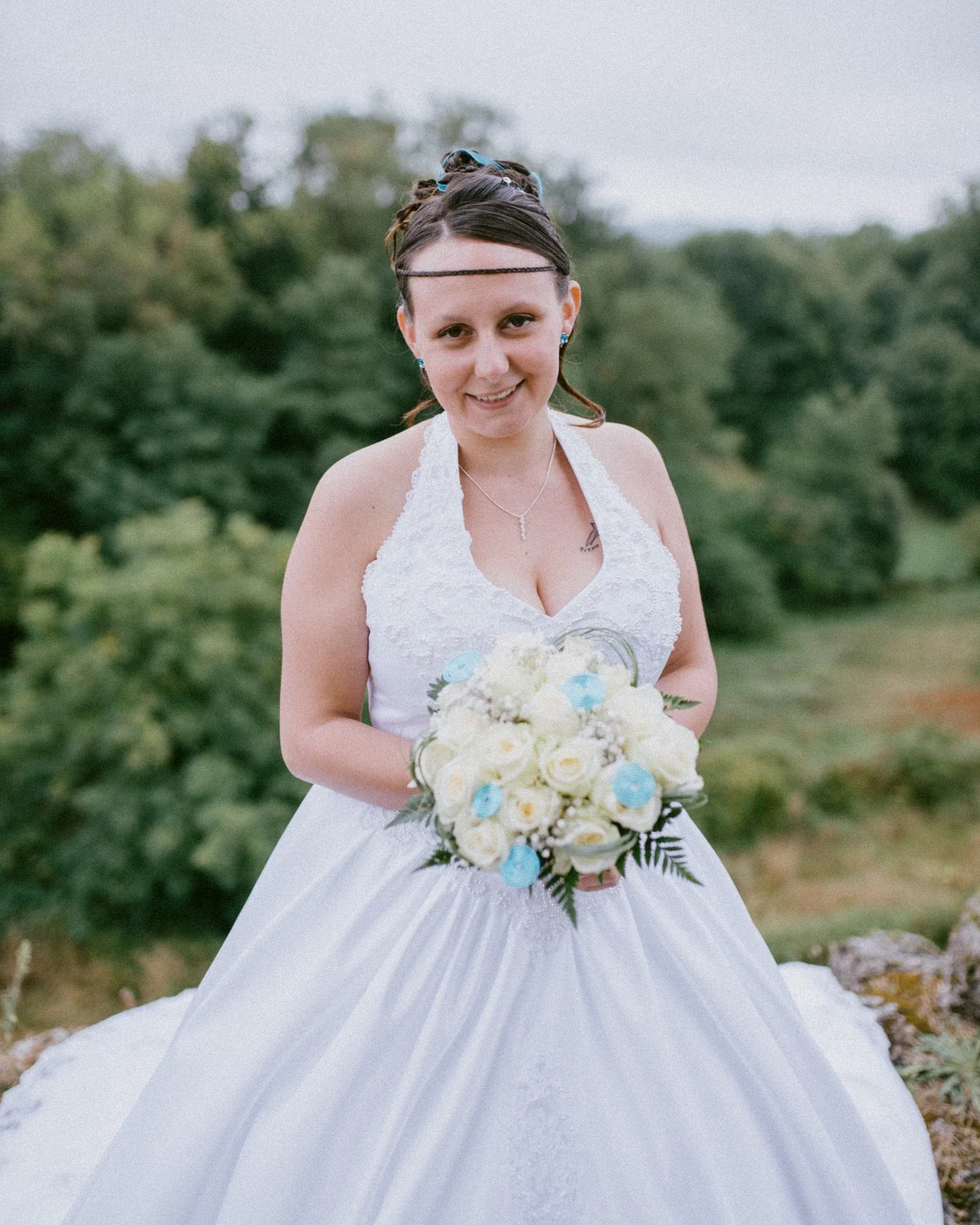 Portrait de la mariée en robe dos-nu brodée, tenant un bouquet de roses blanches et de touches turquoise