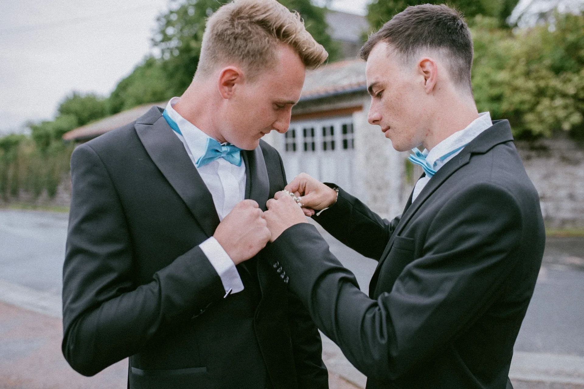 Un témoin en nœud papillon turquoise épinglant la boutonnière de fleurs blanches sur la veste du marié