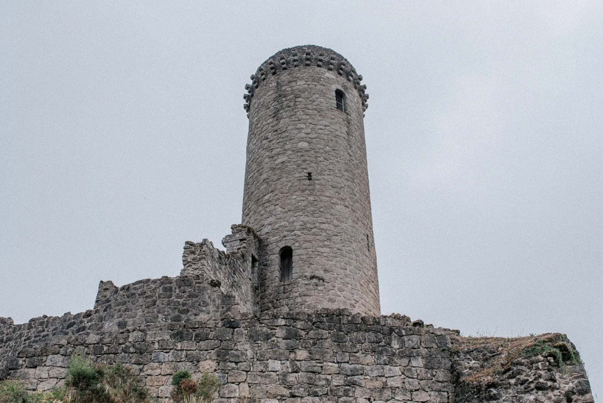La tour ronde en pierre et les remparts en ruines de Piégut-Pluviers sous un ciel gris