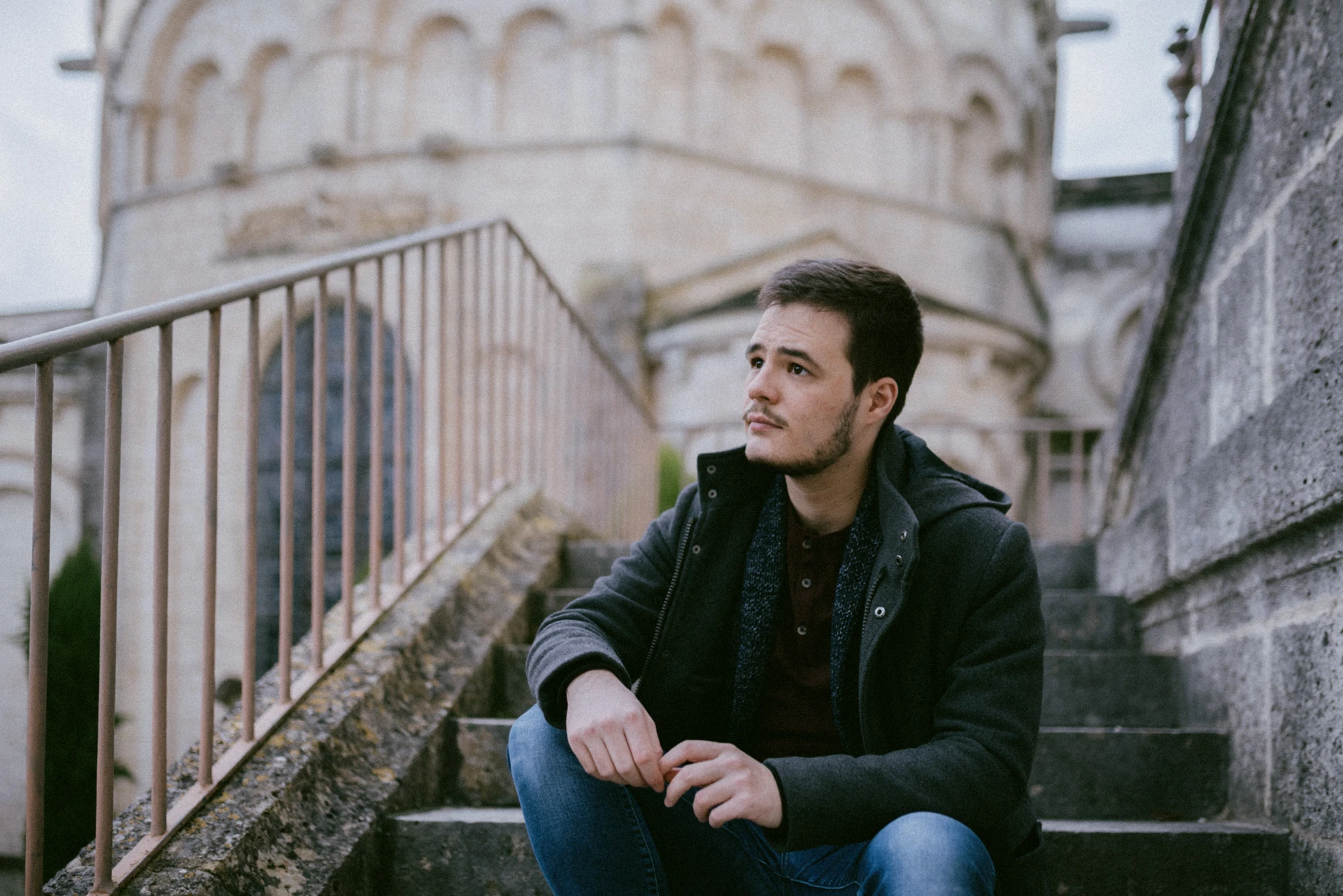 Portrait d'un comédien assis sur des marches de pierre, le regard au loin, devant les arcatures d'un édifice roman à Angoulême