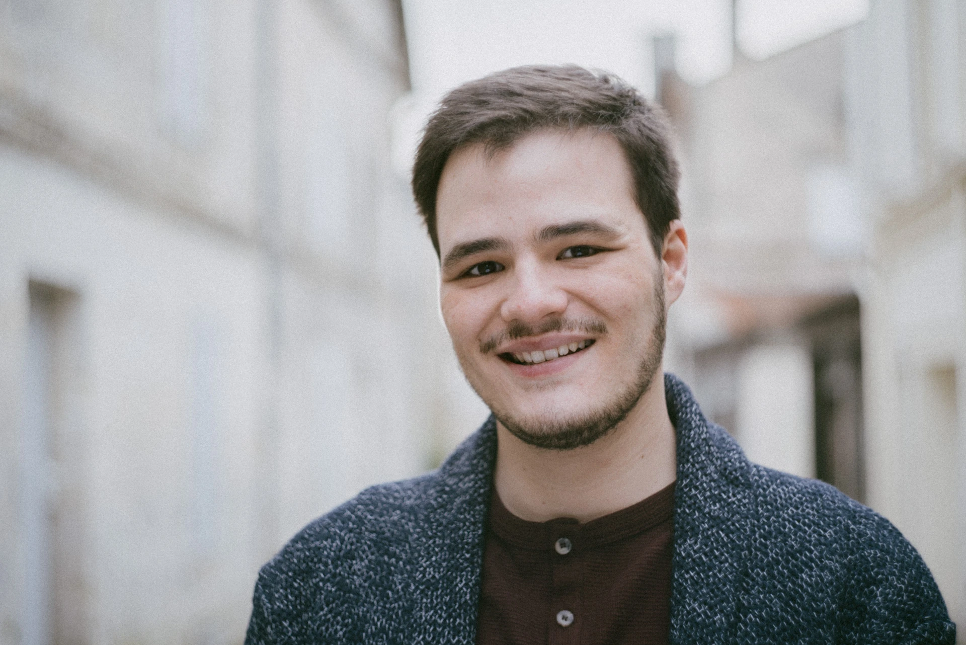 Gros plan d'un comédien au grand sourire, gilet bleu chiné, dans une rue claire d'Angoulême