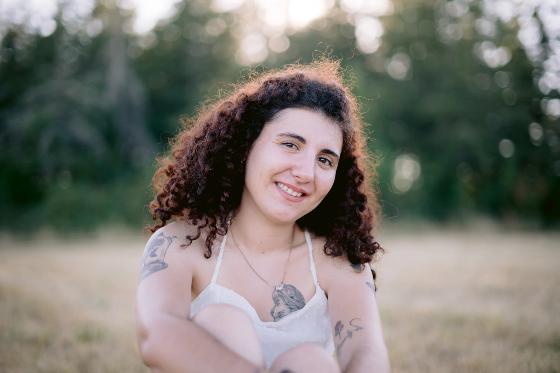 Dernier portrait rapproché d'une jeune femme aux volumineux cheveux bouclés souriant à l'objectif, son tatouage de lion sur la poitrine visible, lors de la séance photo à Écuras en Charente par Alexandre Topolewski