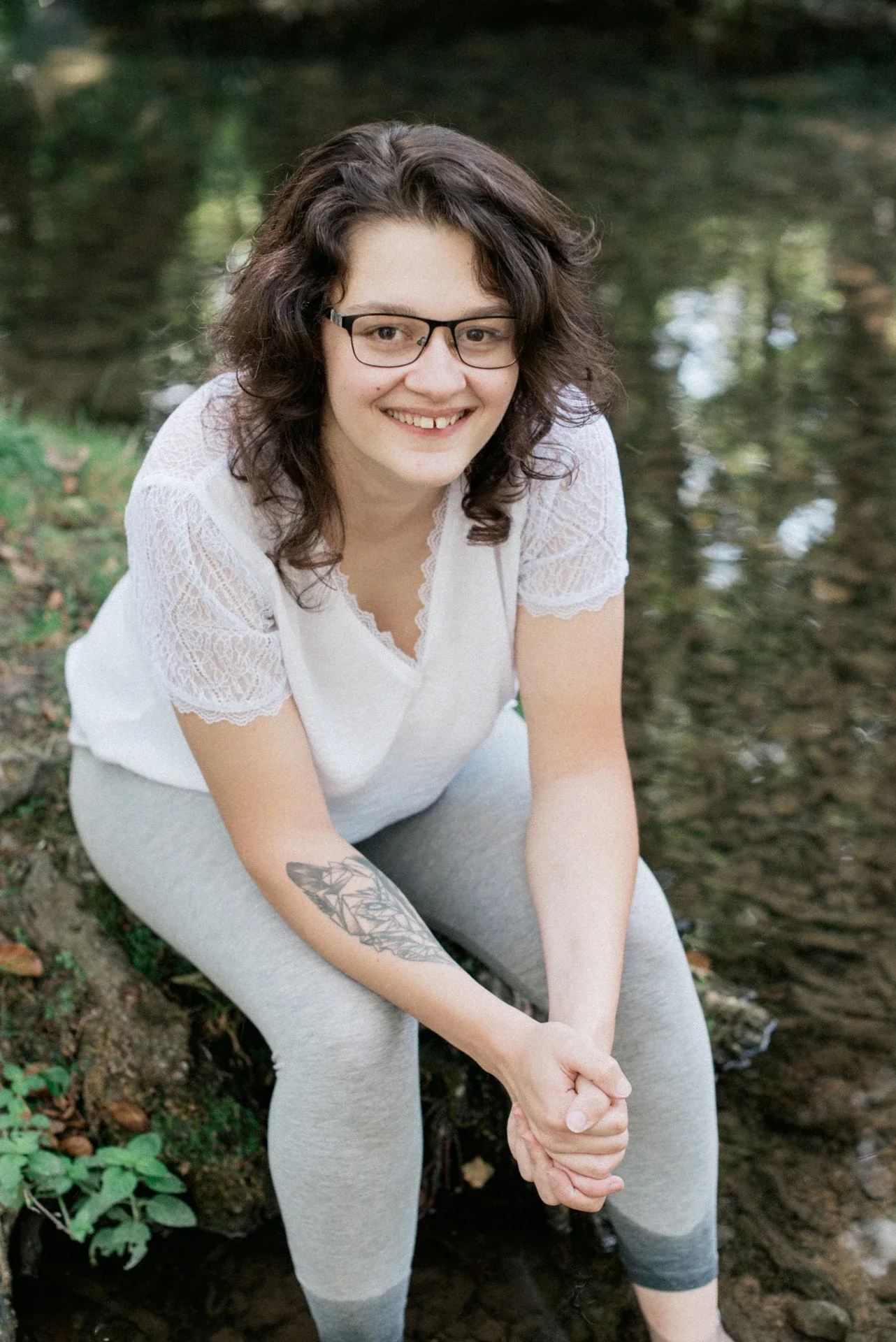 Portrait en plongée légère d'une jeune femme penchée en avant, les mains jointes, au-dessus de l'eau et de ses reflets verts au Lac du Causse