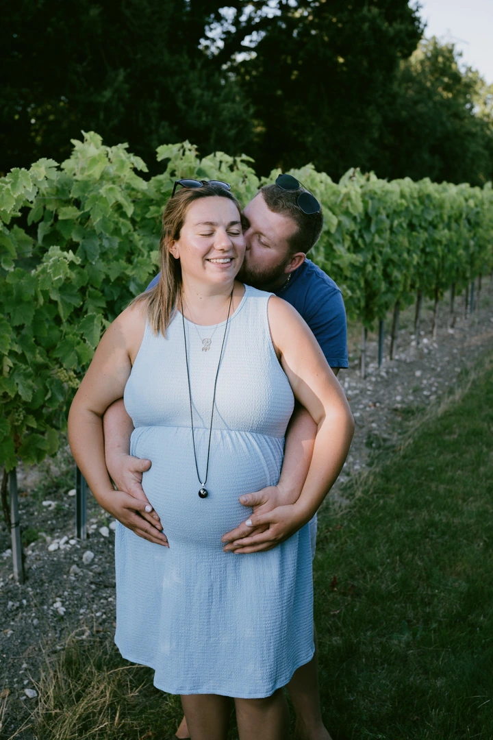 Futur papa embrassant la joue de sa compagne qui sourit, les mains posées sur son ventre