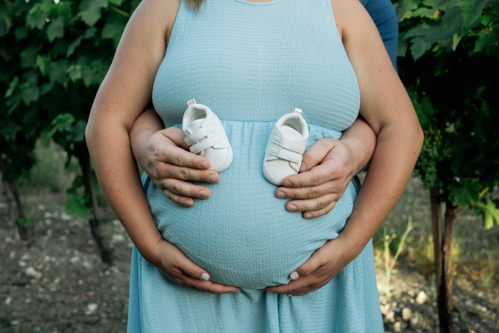 Les chaussons de bébé tenus par les mains du couple sur le ventre arrondi de la future maman