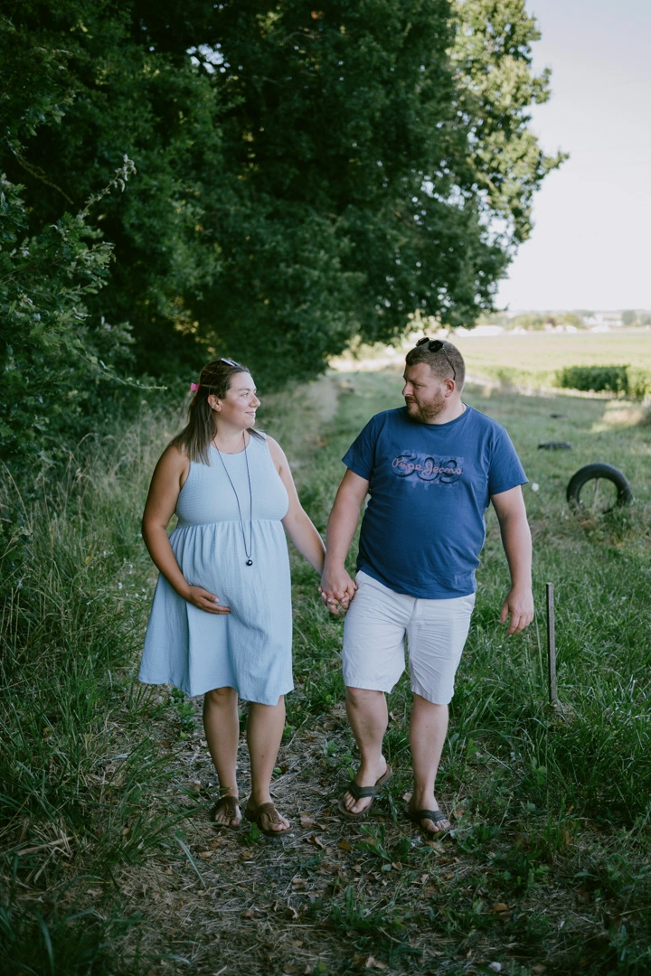 Futurs parents main dans la main, marchant sur un chemin herbeux à Barbezieux-Saint-Hilaire en Charente