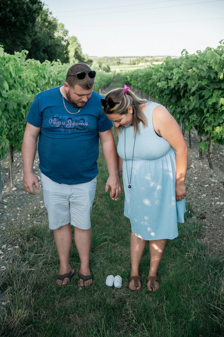 Le couple, tête baissée, regardant les petits chaussons posés devant eux entre les rangs de vigne