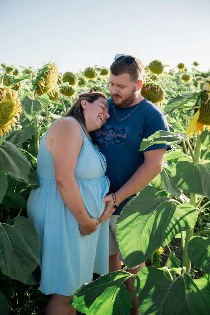 Couple enlacé au milieu des tournesols, la future maman la tête posée sur l'épaule de son compagnon