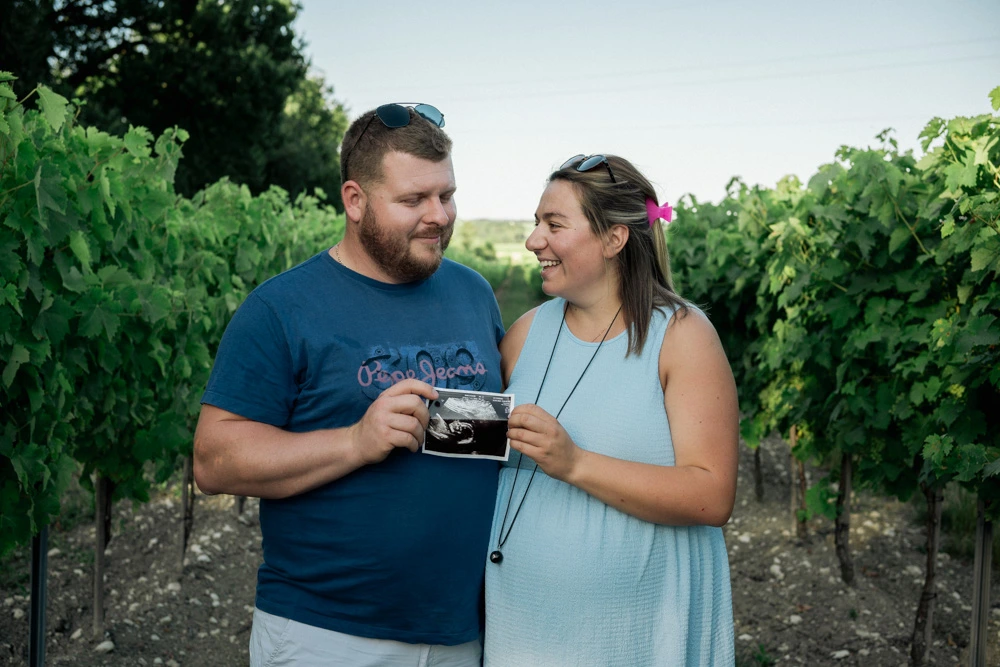 Futurs parents souriants tenant ensemble l'échographie de leur bébé entre les rangs de vigne