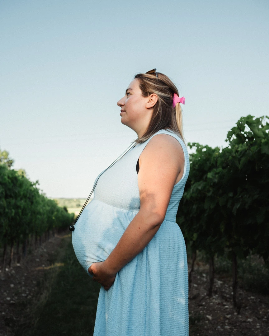 Portrait de profil de la future maman, la main sous son ventre, dans les rangs de vigne