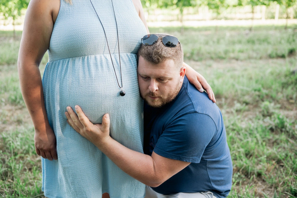 Futur papa blotti contre le ventre de sa compagne, l'oreille posée pour écouter bébé
