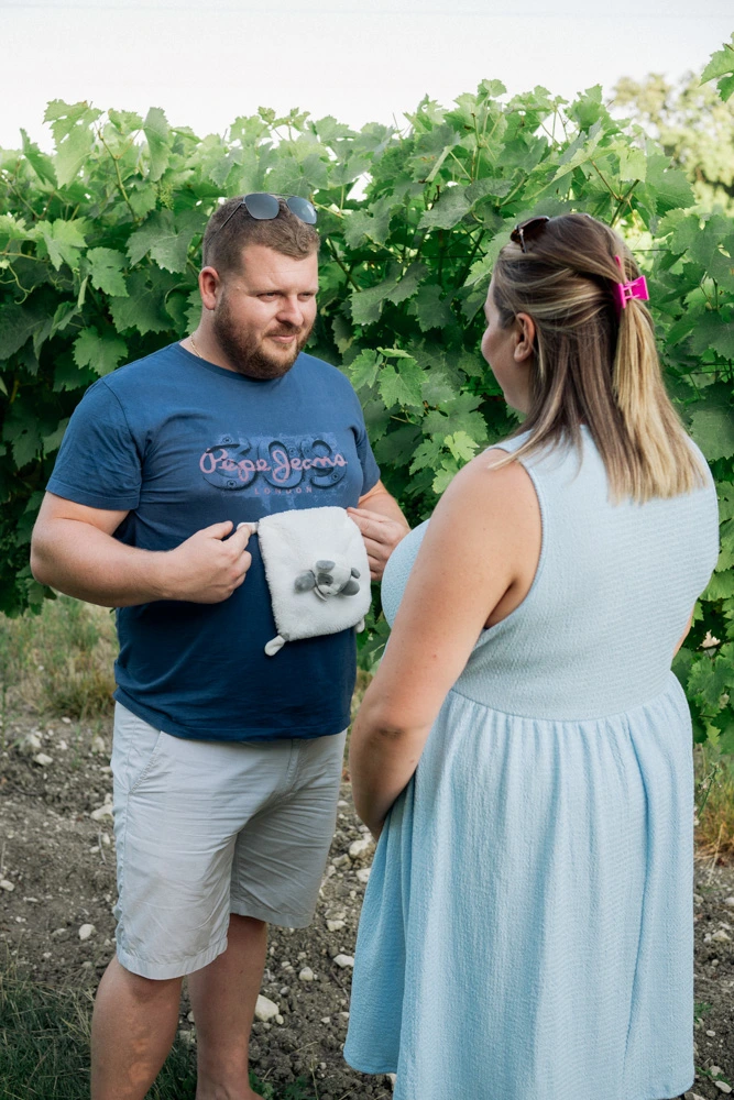 Futur papa posant le doudou sur son t-shirt face à sa compagne, dans les vignes