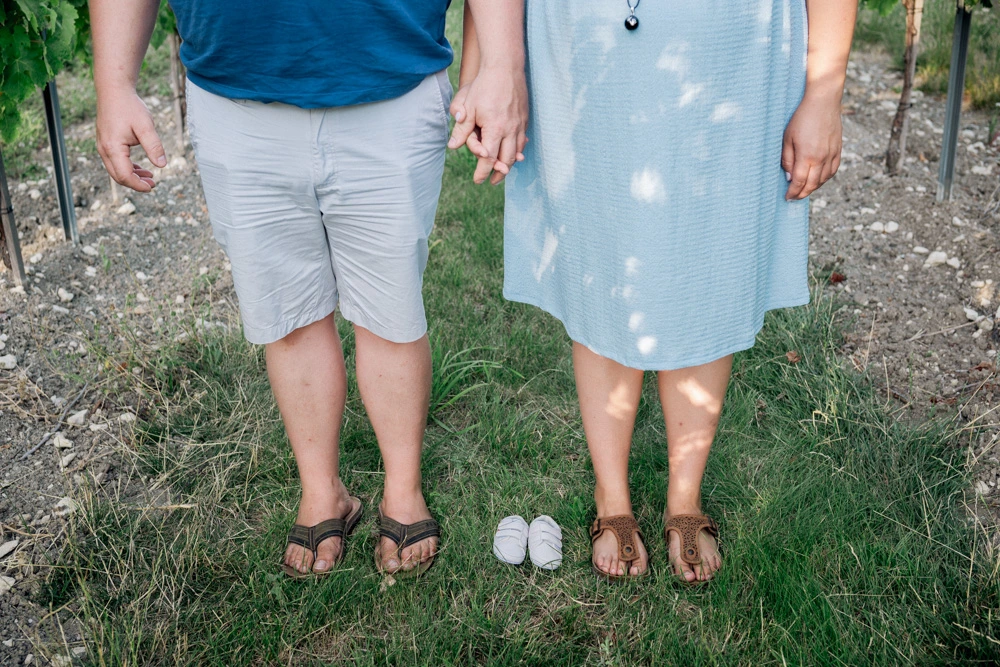 Les pieds du couple côte à côte dans l'herbe, avec une paire de chaussons de bébé entre eux
