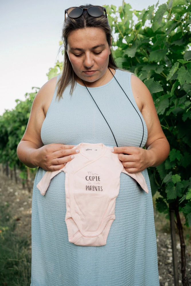 Portrait de la future maman tenant le body de bébé contre son ventre, le regard baissé