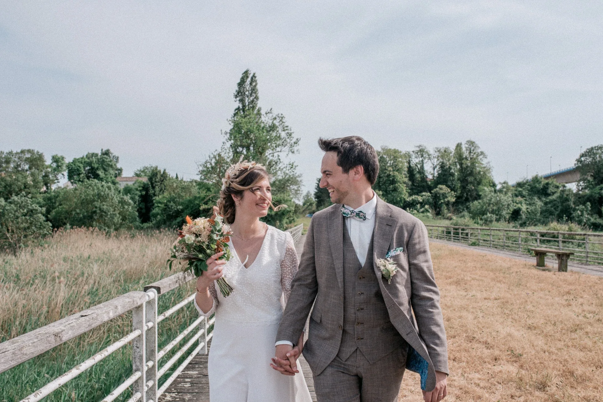 Mariés qui se tiennent la main et se sourient sur un ponton près de Rochefort, mariage en Charente-Maritime