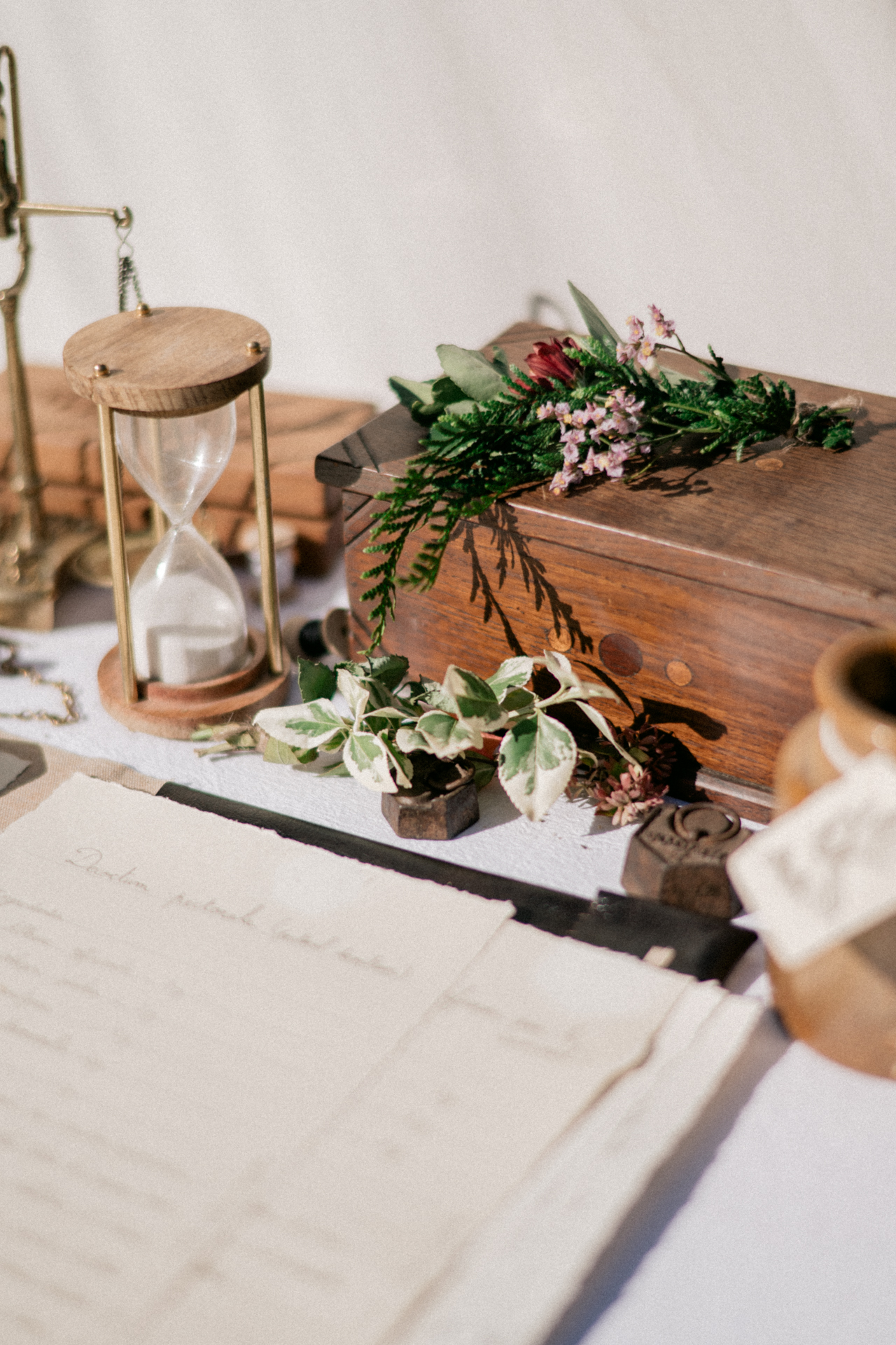 Détails de décoration de mariage vintage à Bordeaux – composition florale, sablier ancien et papeterie élégante sur table lumineuse.