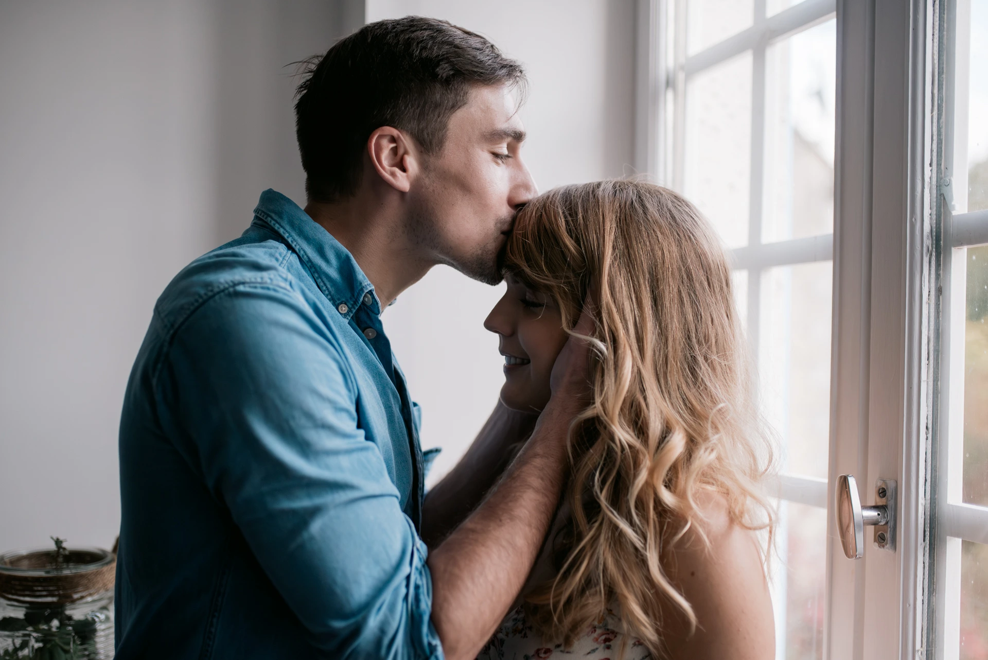 Moment tendre entre un couple près d’une fenêtre, lumière naturelle, séance photo couple à Bordeaux