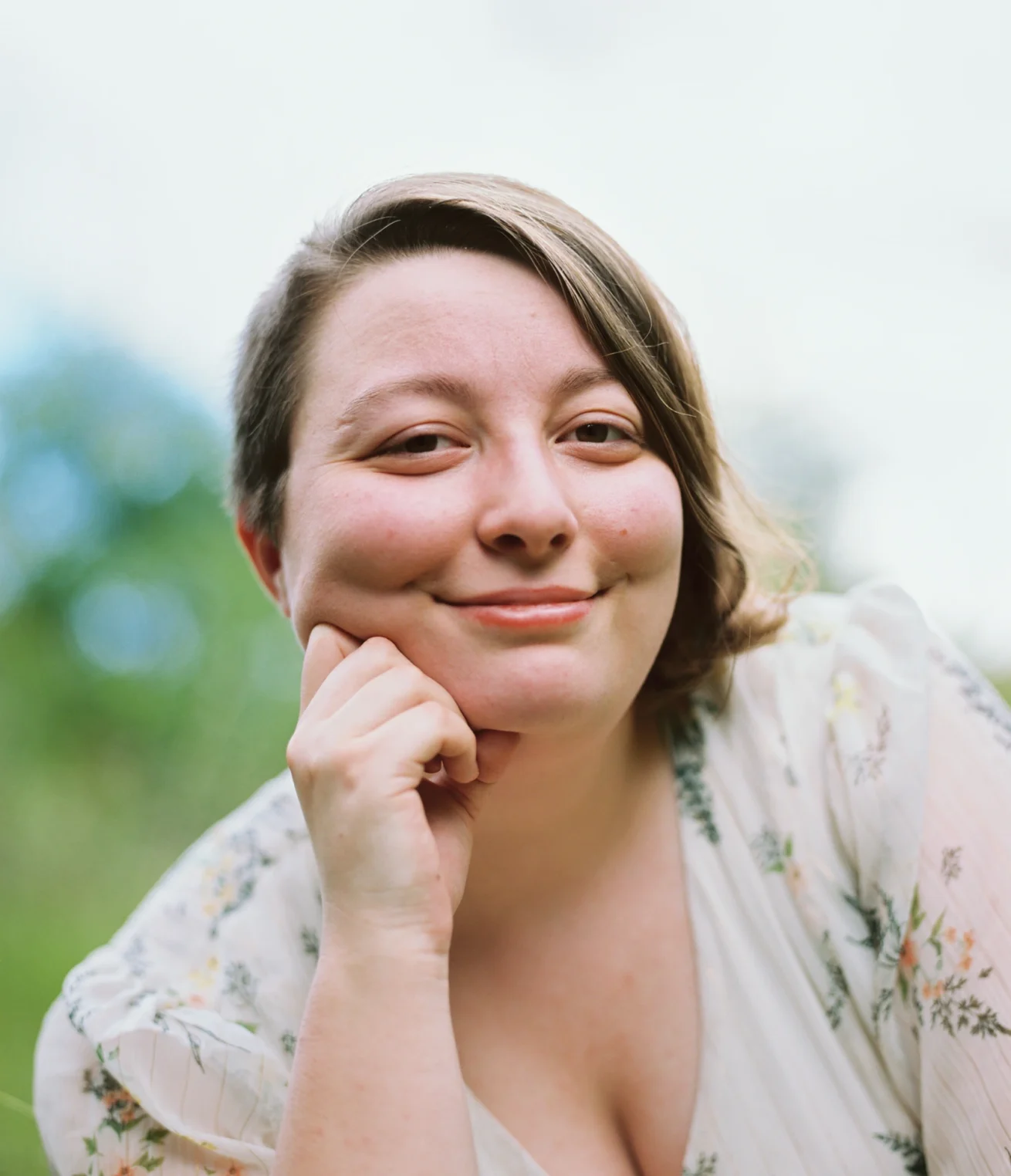 Portrait argentique d'une femme souriante, appuyée sur sa main, fond végétal flou – photographie Fine Art par Alexandre Topolewski, Angoulême