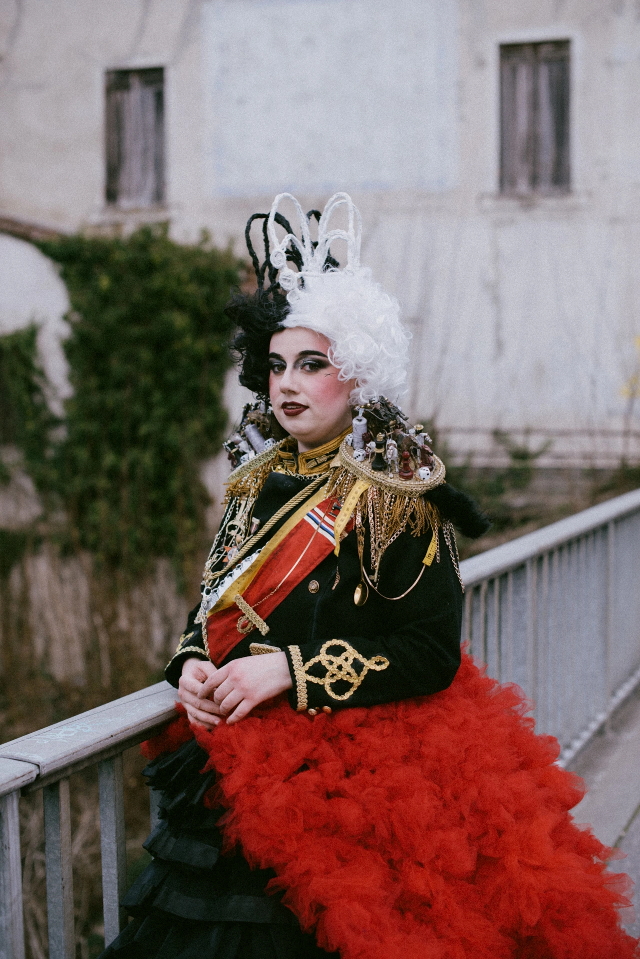 Portrait de trois-quarts cosplay Cruella, garde-corps métallique, jupon rouge, séance éditoriale Dordogne