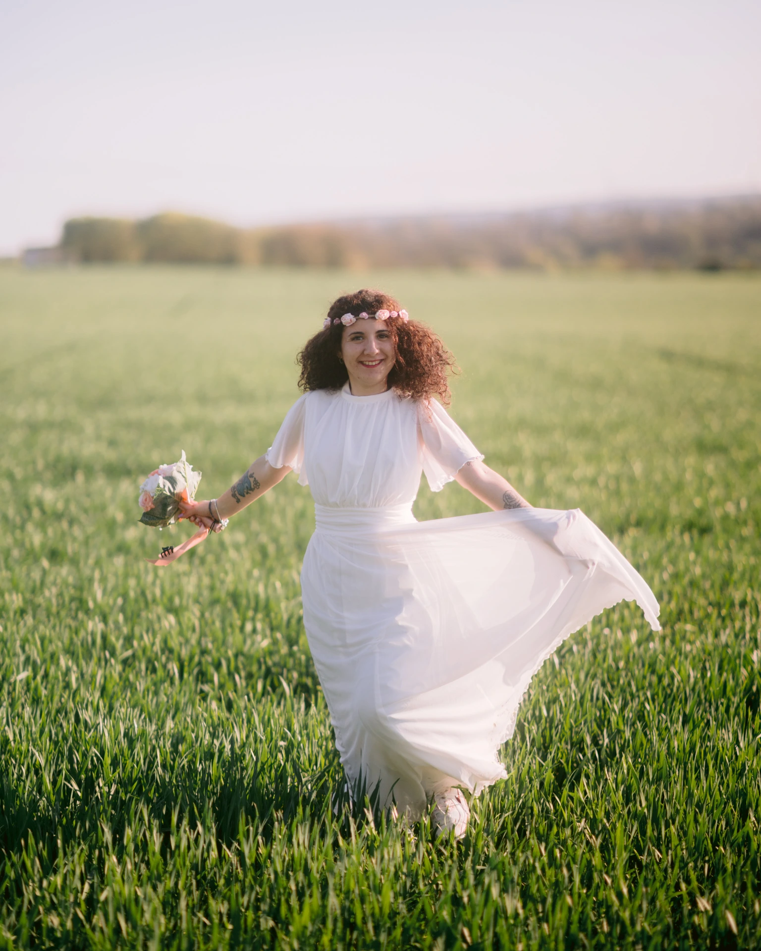 Séance photo lumière naturelle Ruffec Charente - portrait femme en mouvement dans un champ vert avec couronne de fleurs et robe blanche au coucher du soleil