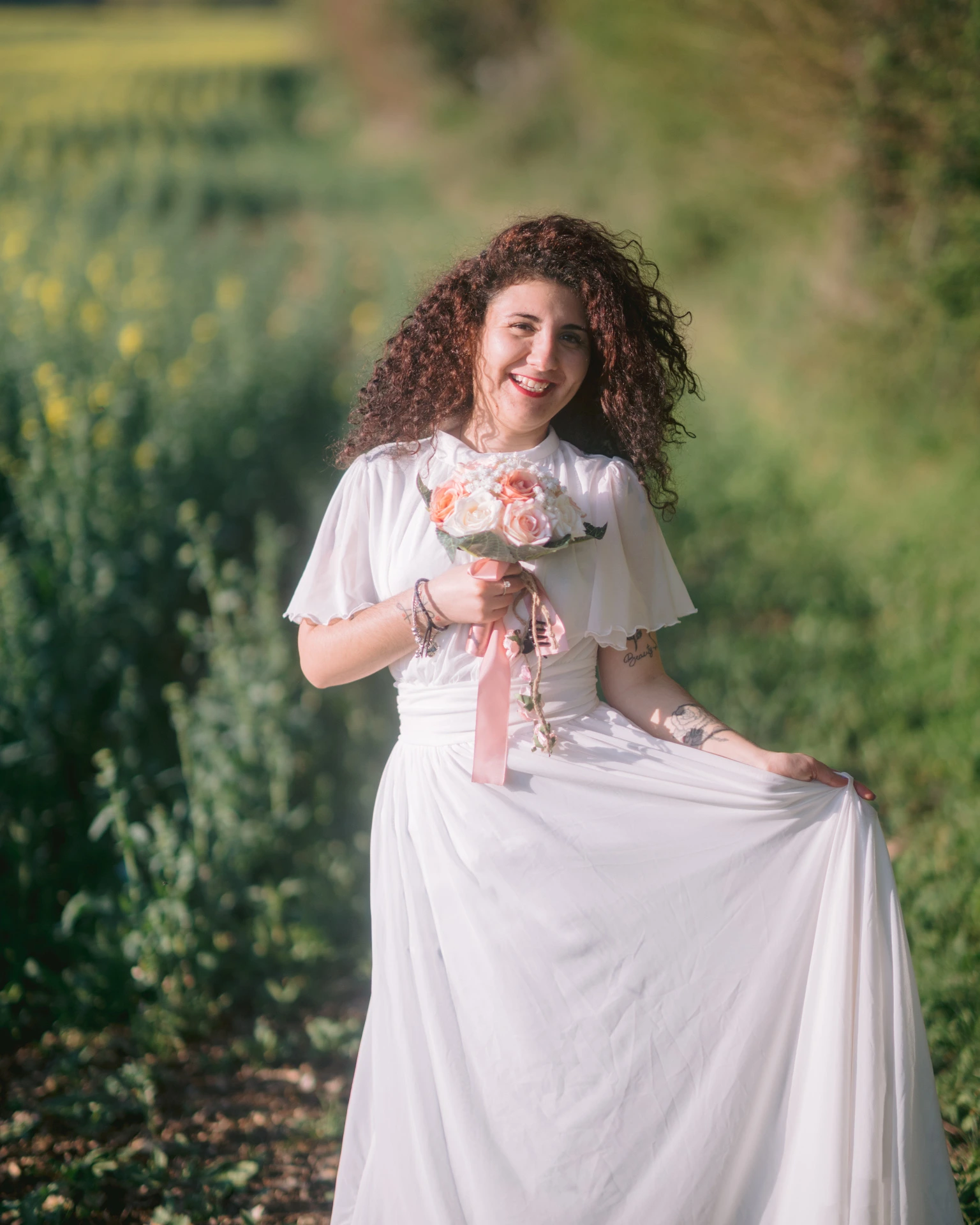 Photographe portrait Ruffec Charente - jeune femme en robe blanche fluide tenant un bouquet pêche et rose dans un chemin verdoyant à l'heure dorée