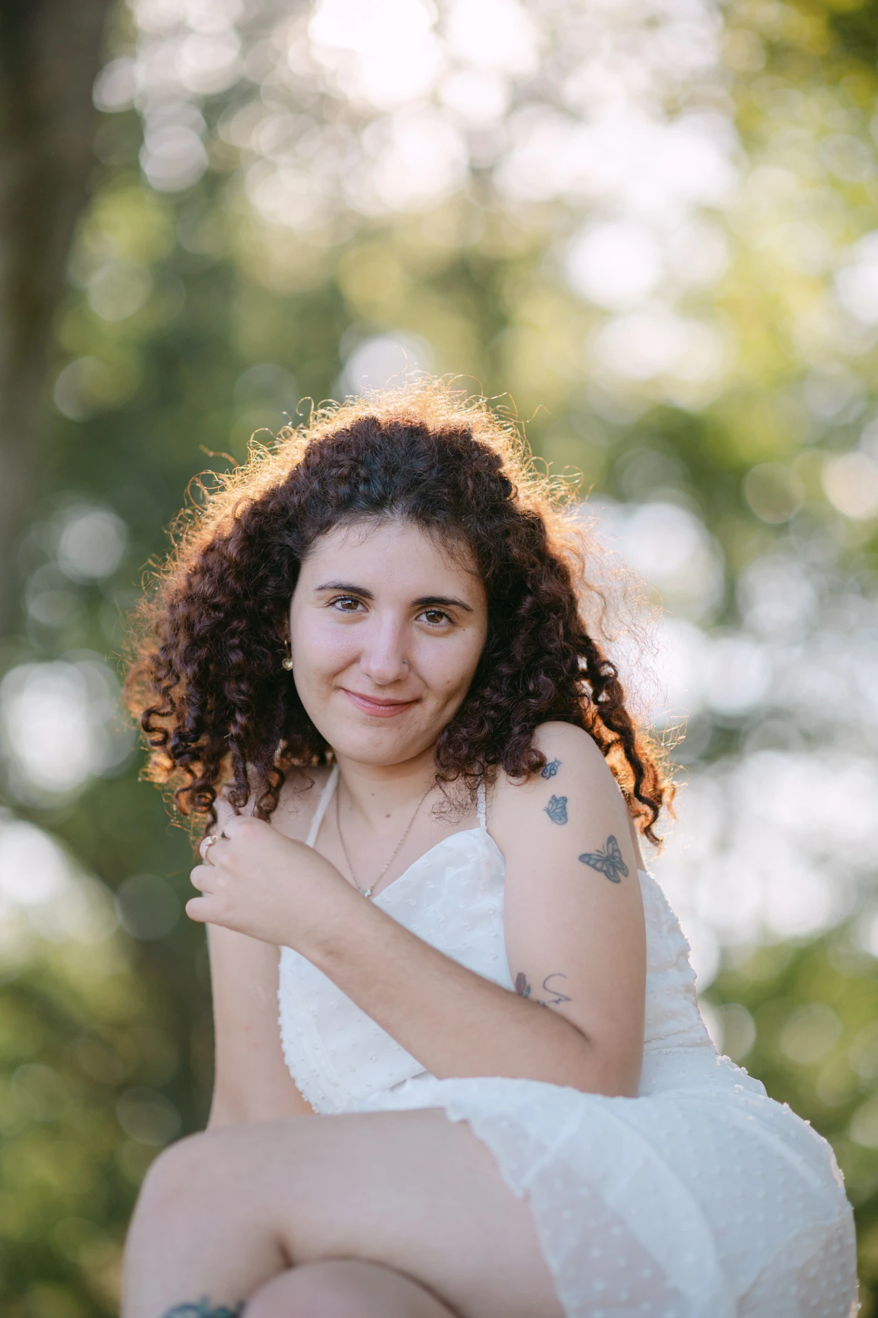 Portrait fine art d'une jeune femme aux cheveux bouclés et sourire naturel, robe blanche, contre-jour doré en forêt à Écuras en Charente