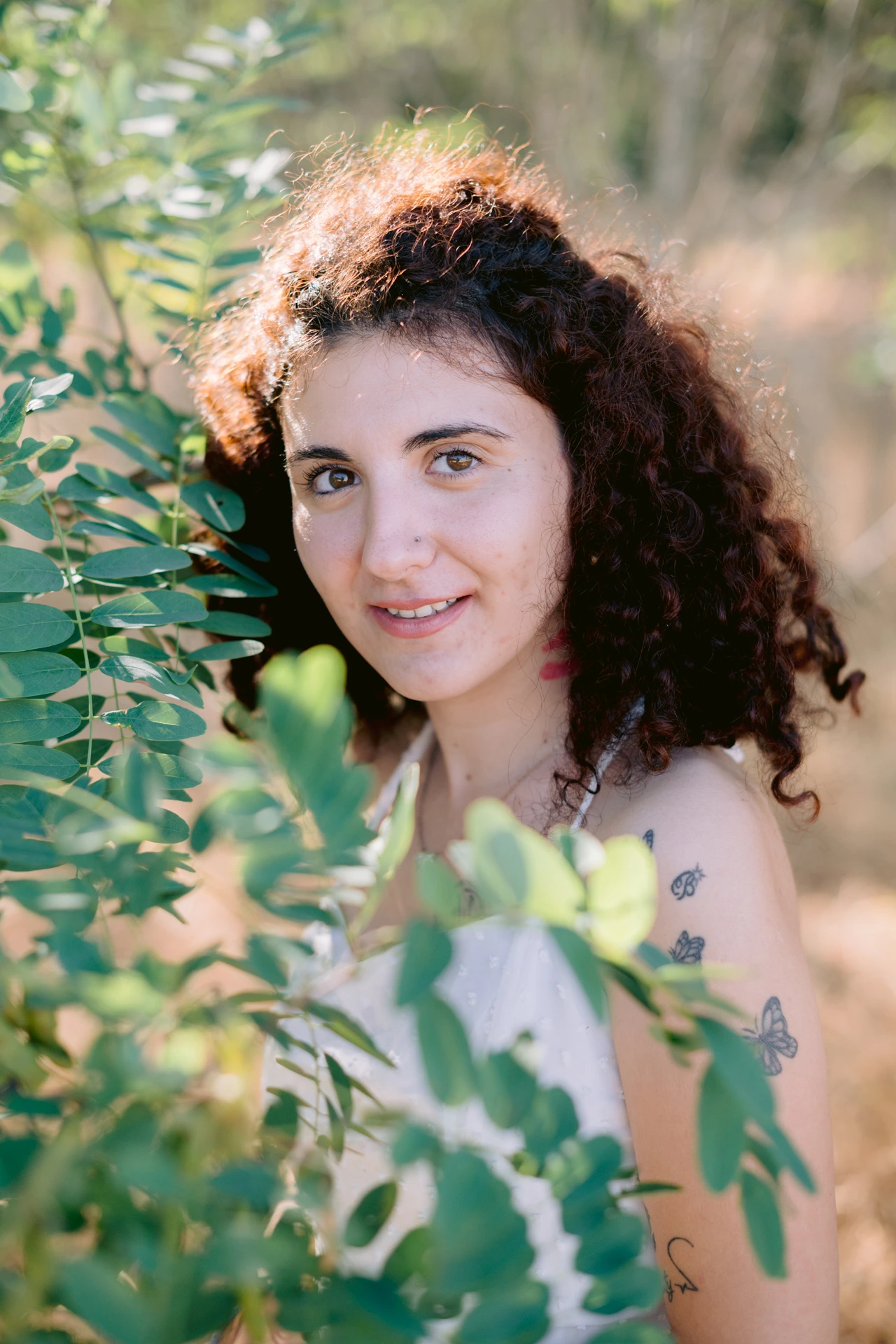 Portrait fine art rapproché d'une jeune femme aux cheveux bouclés souriante, encadrée de feuillage vert, à Écuras en Charente