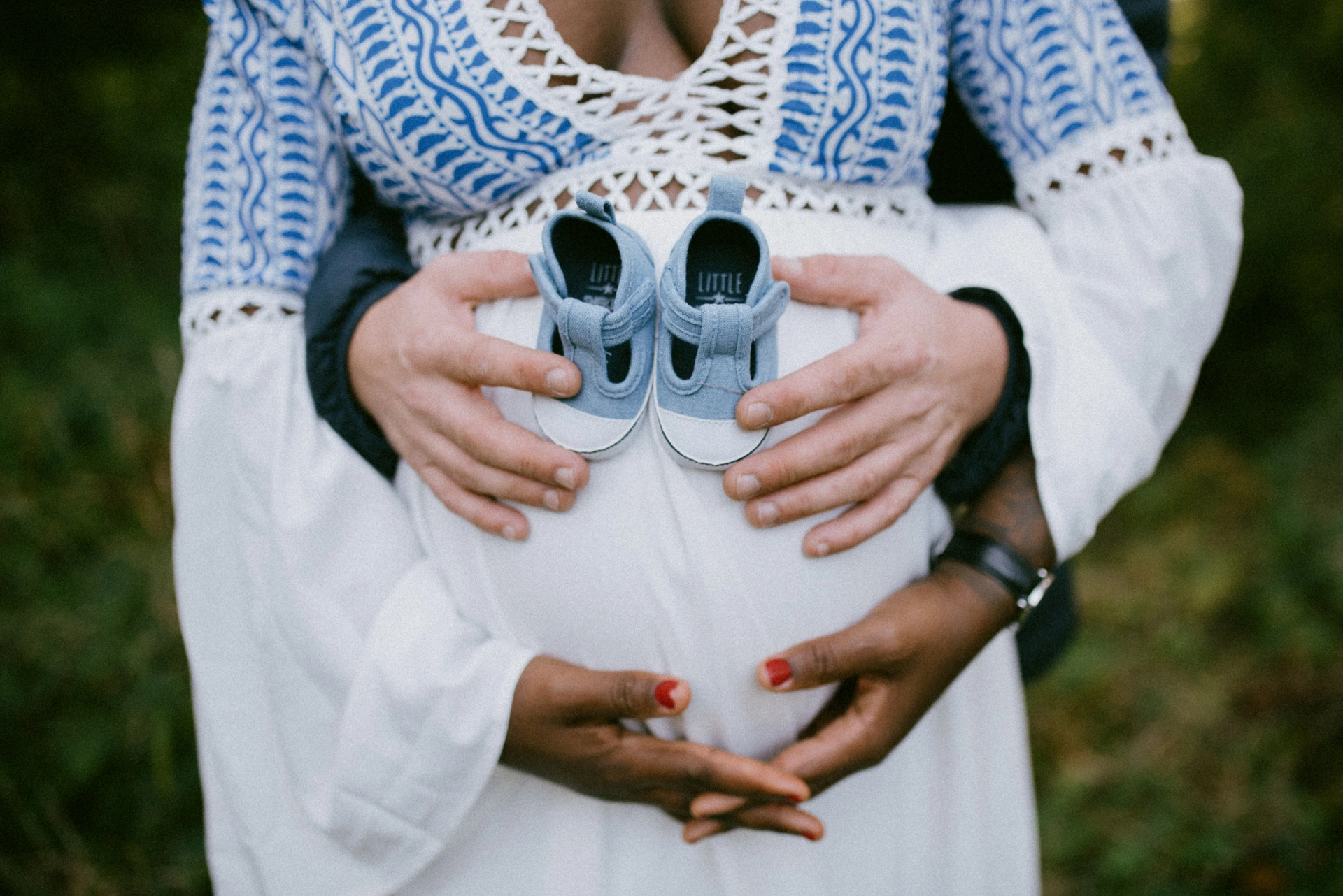 Mains des futurs parents tenant de petits chaussons bleus contre un ventre de femme enceinte