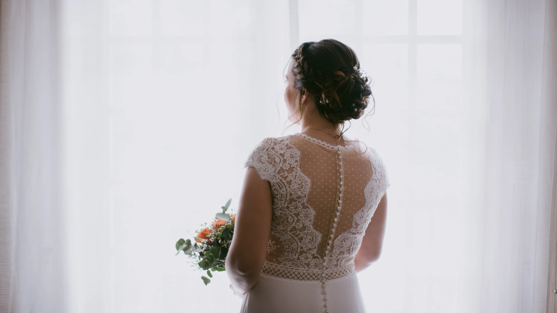 Mariée de dos devant une fenêtre en lumière naturelle, robe en dentelle, Alexandre Topolewski photographe de mariage en Charente